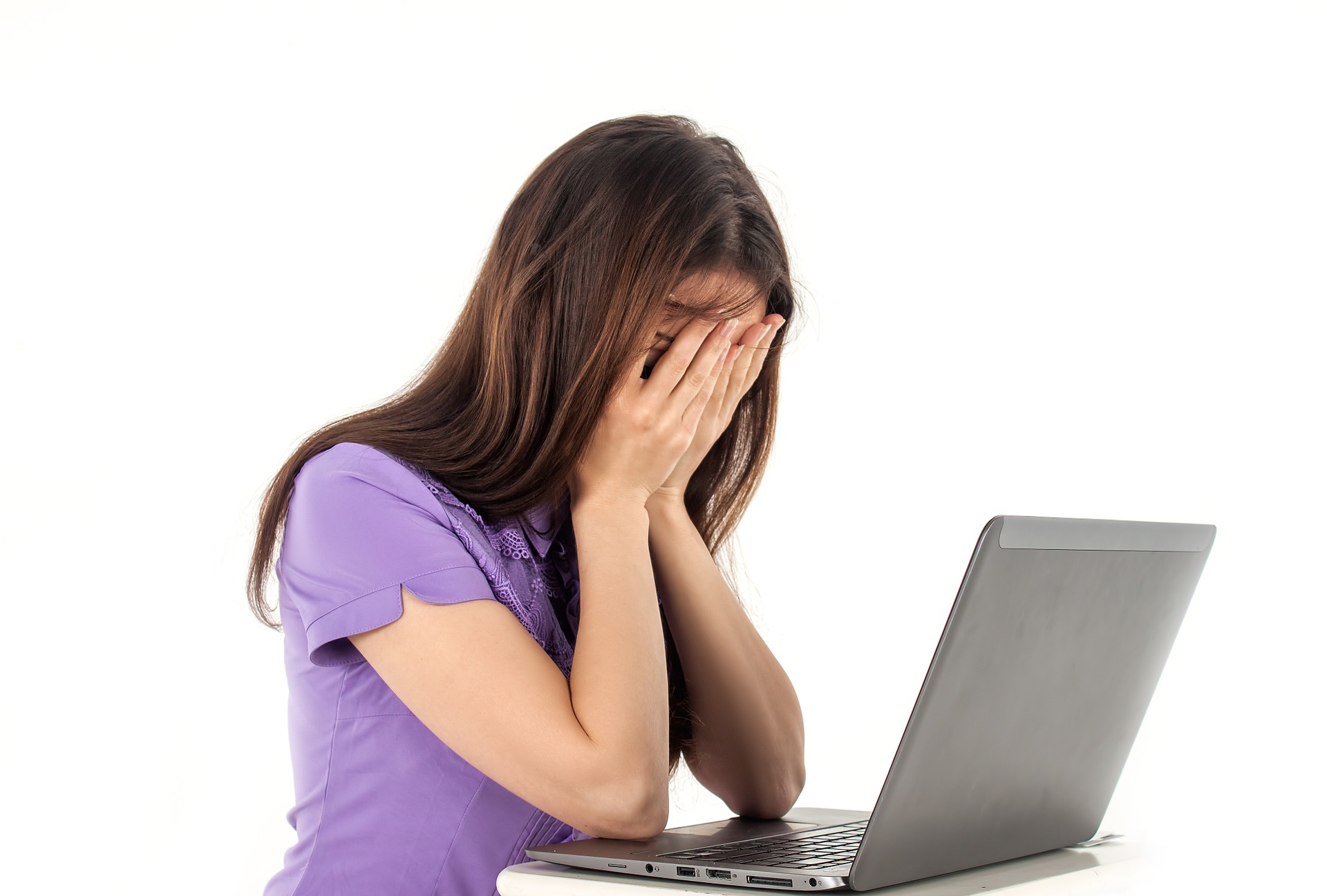 A woman covering her face exasperatedly whilst looking at a laptop